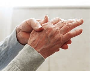 Elderly person massaging their own arthritic hands to relieve the pain and discomfort.