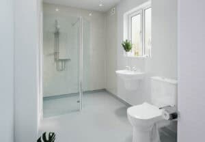 Plain white and simplistic deigned wet room, glass screen covering the side which the shower is mounted on the wall.