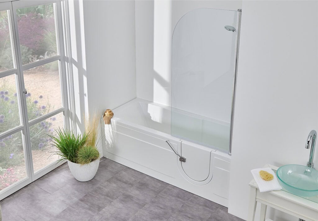 Livorno (Arizona) walk-in shower bath. Long metal leaver to open side door. Large spiky plant in pot next to bath and natural light coming in from right.