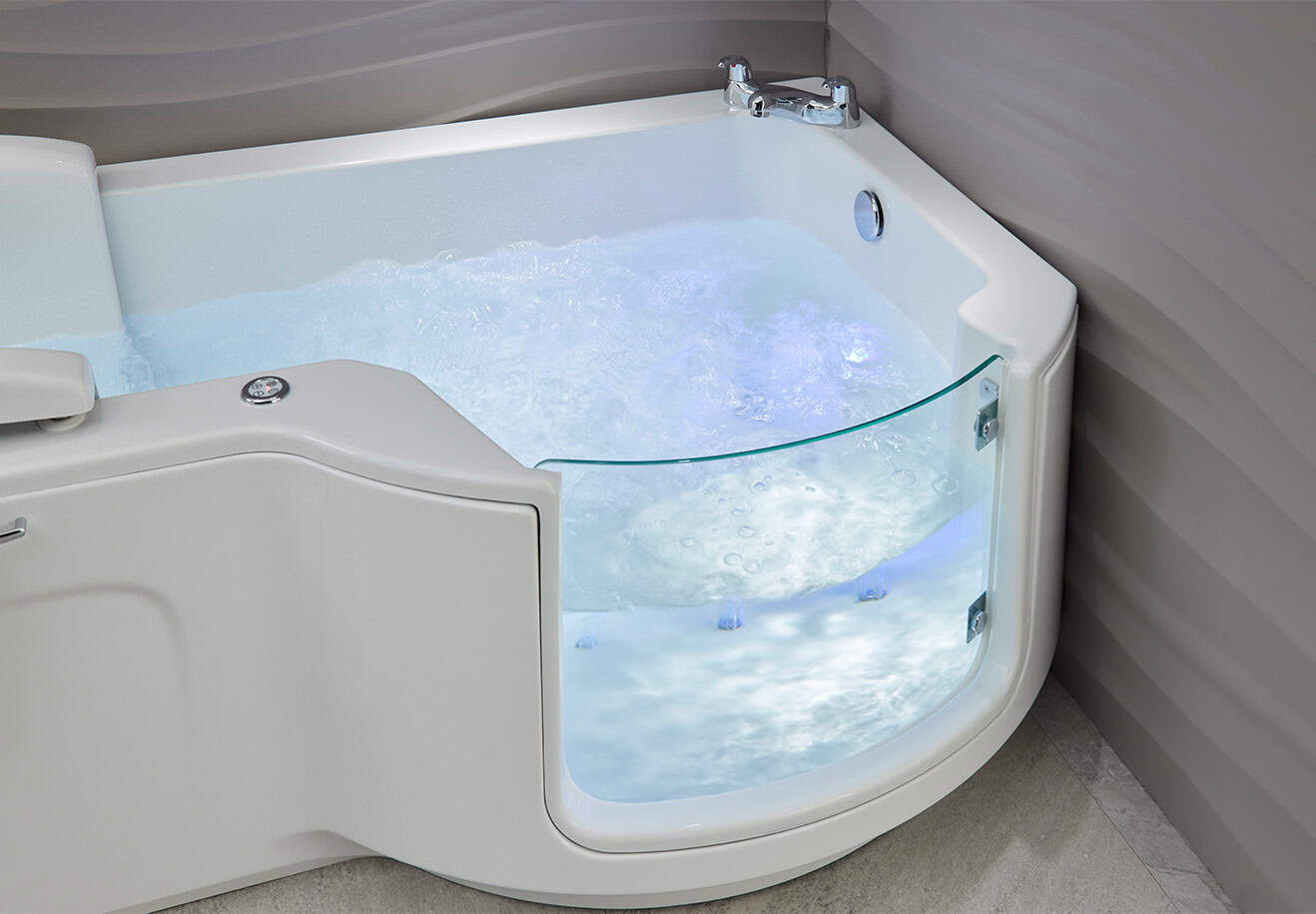 Walk-in bath Roma (Louisiana - access baths) zoomed in half view bath glass door, filled with water and bright blue light illuminating inside of tub. In neutral coloured theme bathroom.