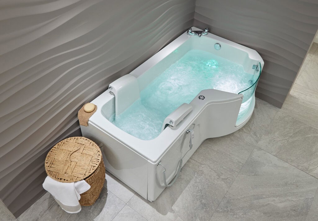 Walk-in bath Roma (Louisiana - access baths) aerial view of full bathfilled with water and bright blue light illuminating inside of filled tub. In neutral coloured theme bathroom.