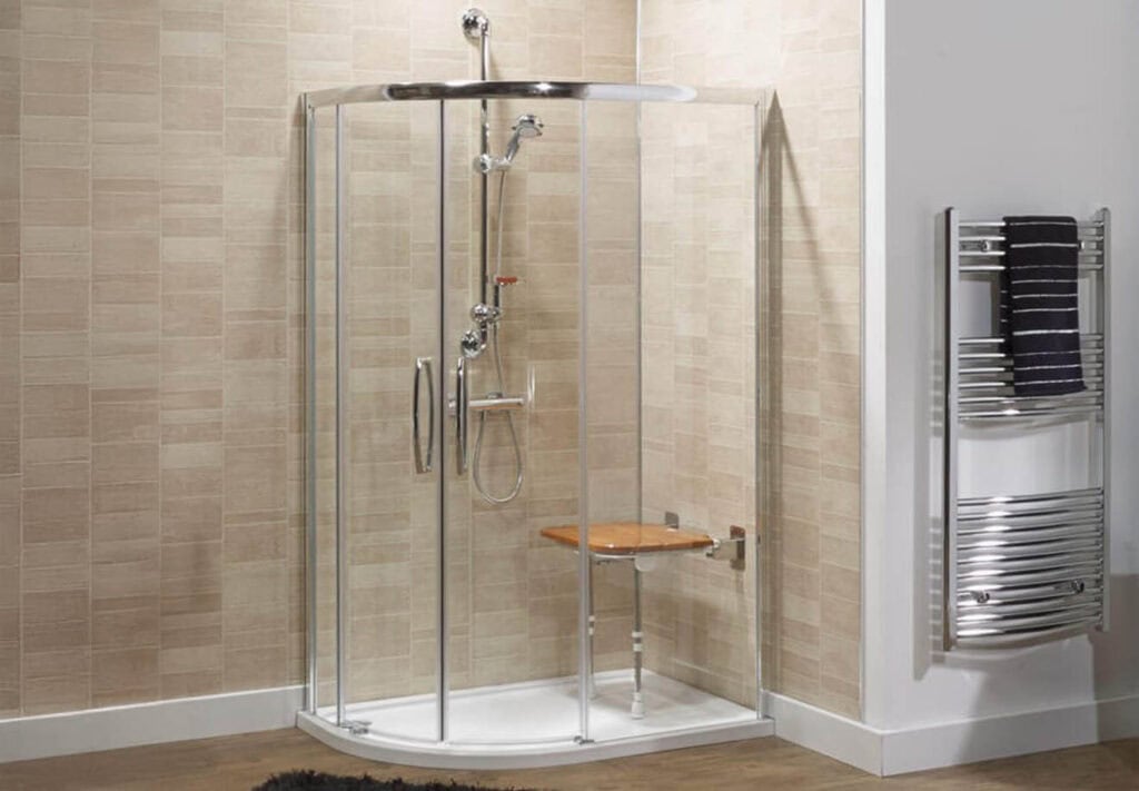 Classic accessible shower enclosure with wall-mounted wooden seat, handheld shower head, and chrome towel radiator on beige tiled walls.